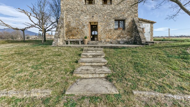 A stone building with a tiled roof, a front door, and a small porch with steps leading to it.