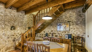 A rustic dining area with stone walls, wooden furniture, a staircase, and a pendant light.