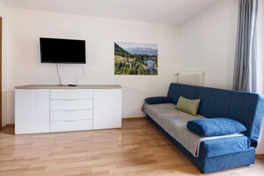 A room with a white cabinet, a blue sofa, a TV, and a landscape painting on the wall.