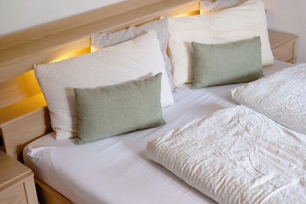 A neatly made bed with white linens and multiple pillows, including a green one, in a well-lit room with wooden headboard and nightstands.