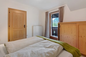 A bedroom with a bed, a wooden wardrobe, a window with curtains, and a radiator.