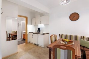 A compact kitchen with white cabinets, a dining area with a wooden table and striped chairs, and a wall clock.