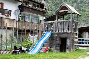 Une construction rustique en bois, dotée d’un toboggan, d’un balcon orné de fleurs et d’un petit véhicule.