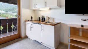 Une cuisine avec des meubles blancs, un plan de travail en bois, une machine à café et un téléviseur fixé au mur.