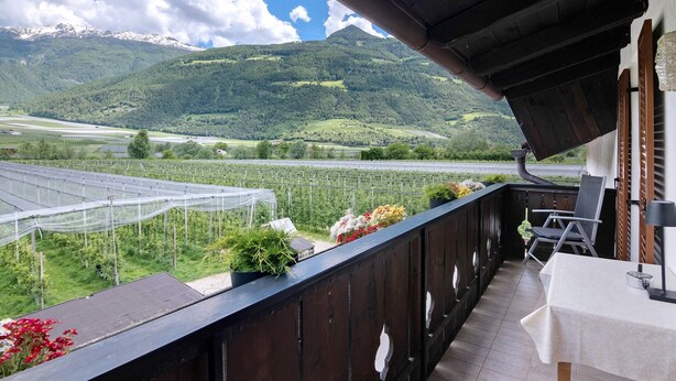 Un balcon avec une table et des chaises, donnant sur une serre et un paysage montagneux.