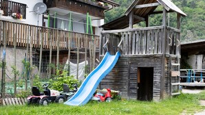 Une construction rustique en bois, dotée d’un toboggan, d’un balcon orné de fleurs et d’un petit véhicule.