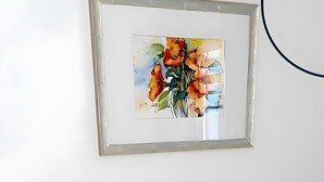 Cama bem arrumada com lençóis e manta brancos, cabeceira de madeira e um quadro emoldurado acima.