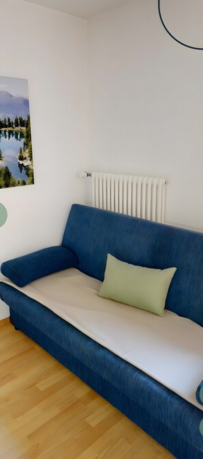 A blue sofa with a light cushion, a radiator, and a painting of a landscape on the wall. - Apartment 'Stark Groß' with Mountain View, Shared Terrace and Wi-Fi (Ciardes)