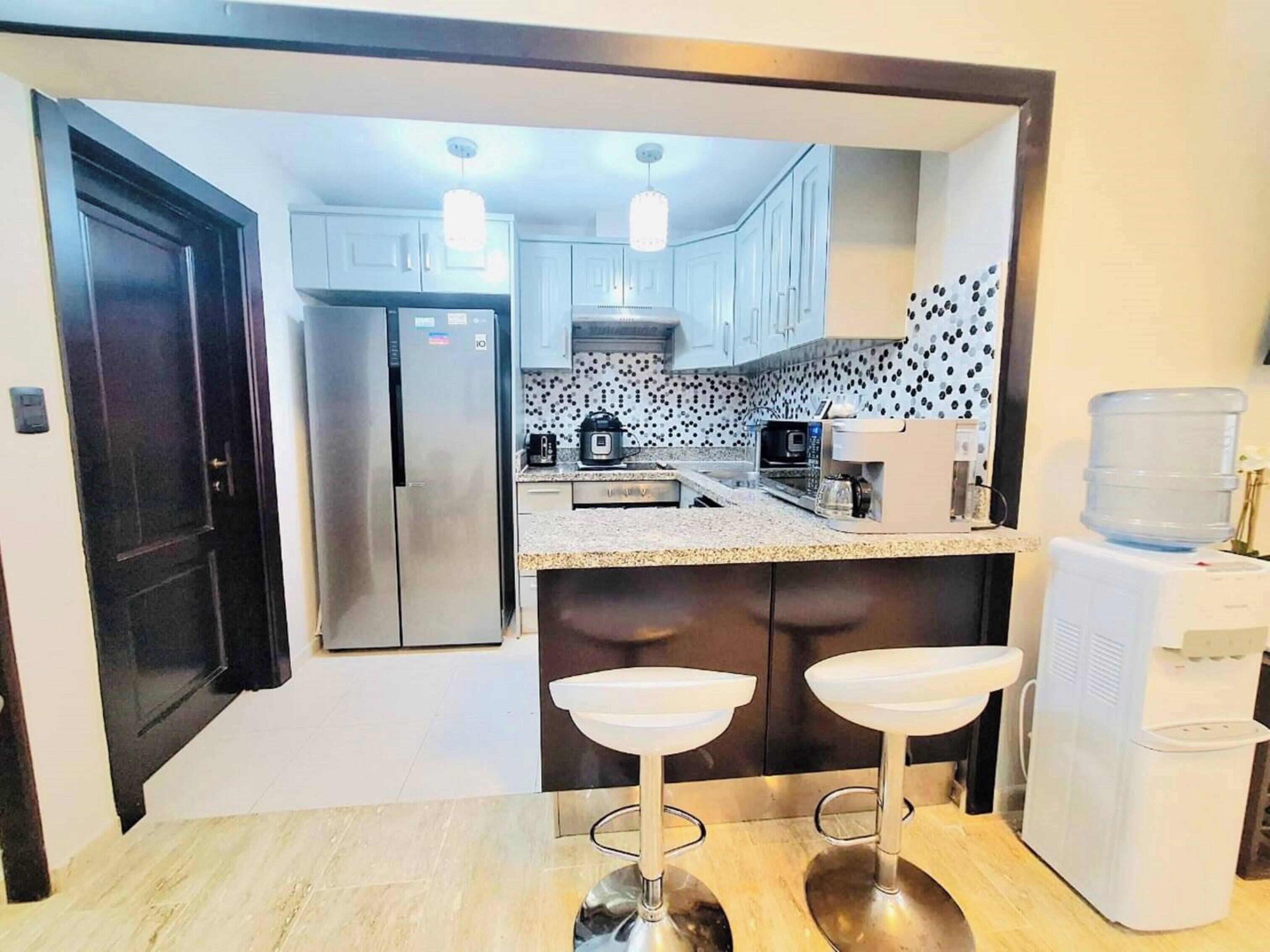 A compact kitchen with a refrigerator, microwave, coffee maker, and water dispenser.