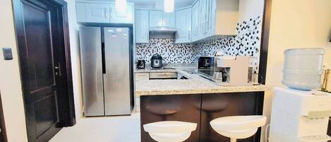 A compact kitchen with a refrigerator, microwave, coffee maker, and water dispenser.