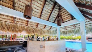 A bar area with a thatched roof, a pool, and a stone counter. - GLOBALSTAY Cocotal Condo in Punta Cana (Punta Cana)