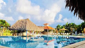 A swimming pool with a thatched-roof structure and a small building in the background. - GLOBALSTAY Cocotal Condo in Punta Cana (Punta Cana)