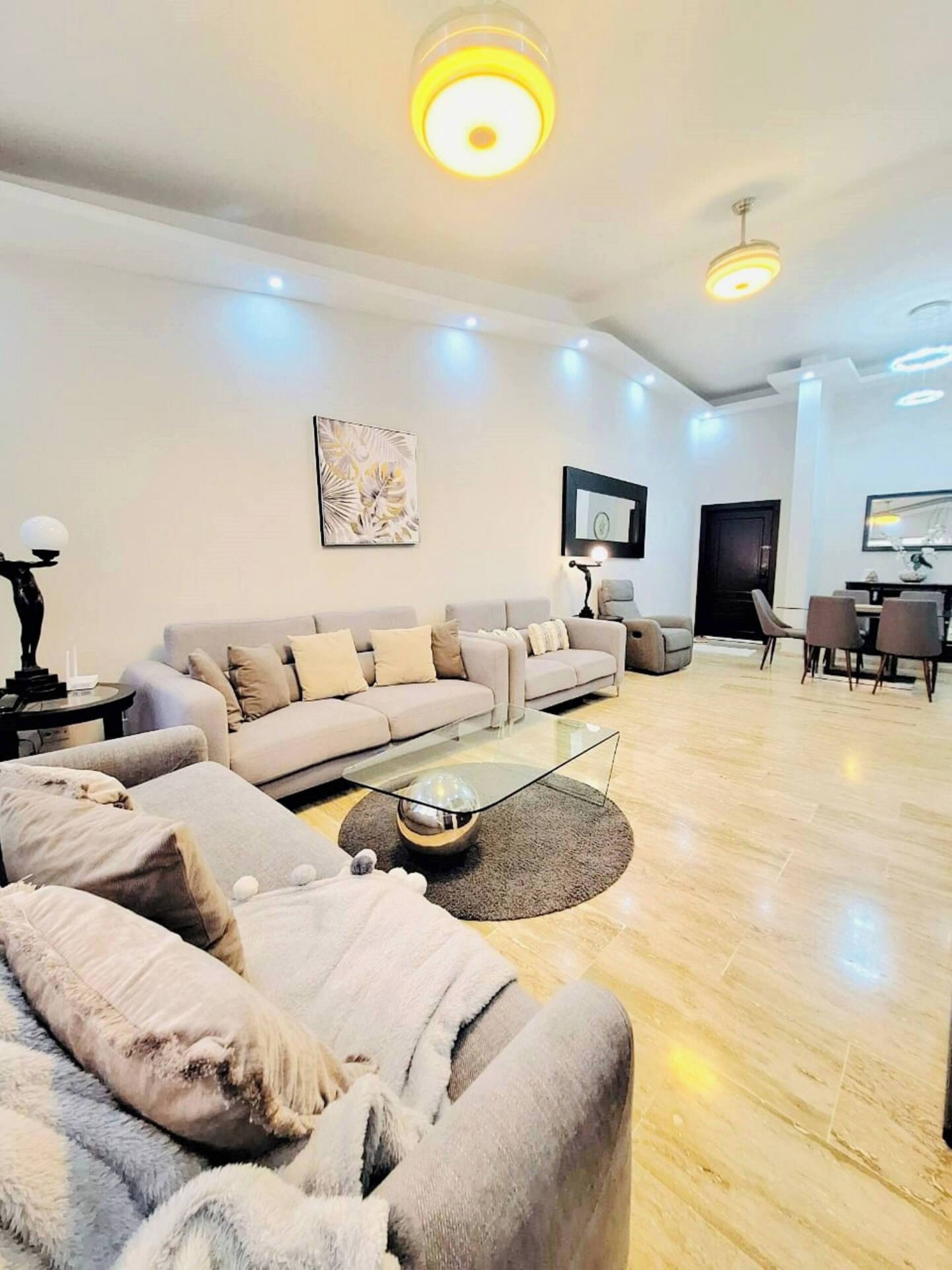 A modern living room with a sofa, coffee table, and a dining area with chairs.