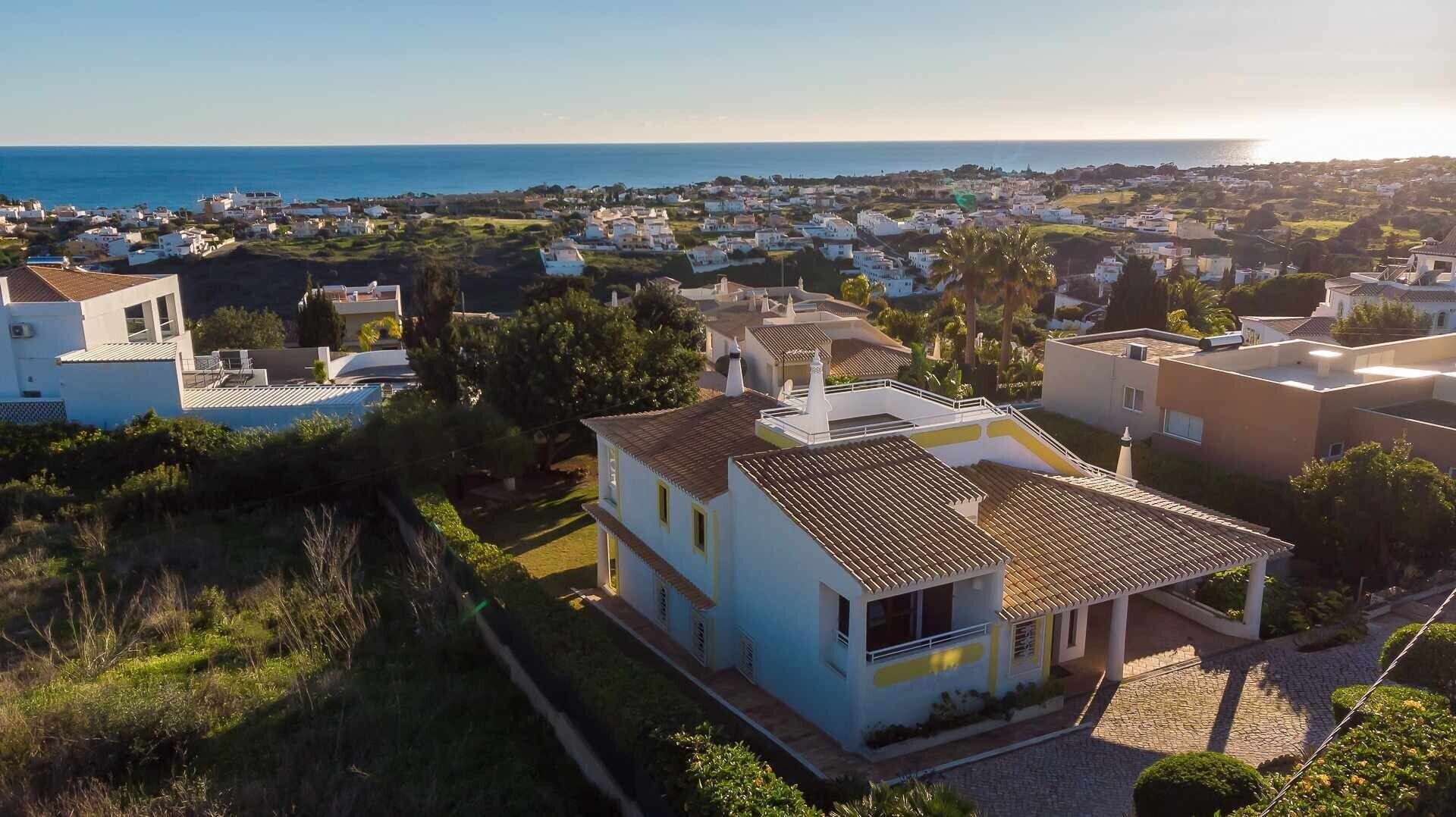 A residential area with houses, a clear view of the sea, and a prominent building with a tiled roof.