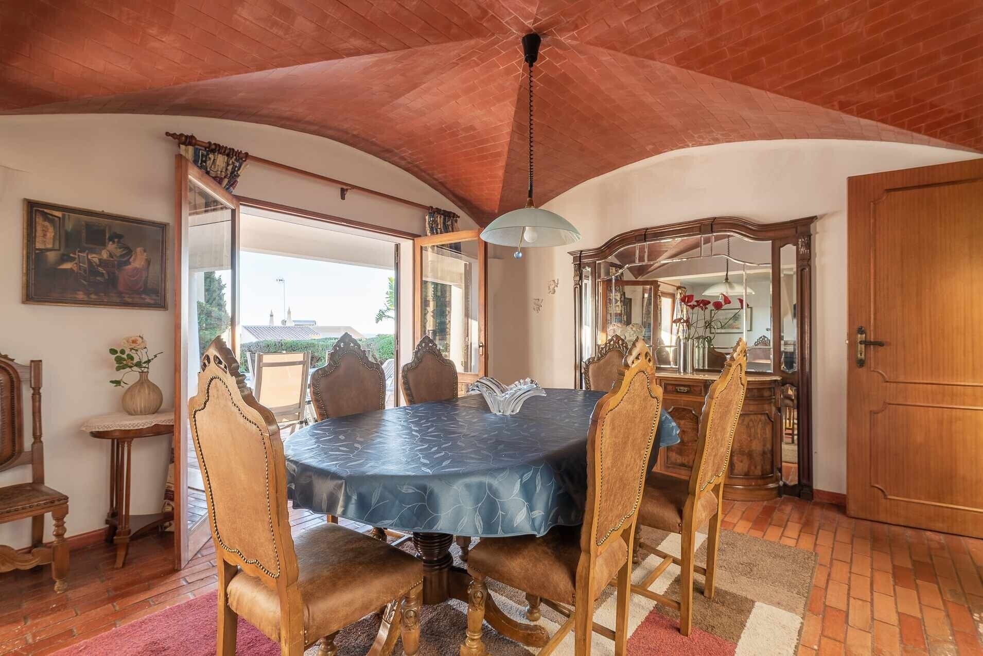 A dining area with a round table, chairs, a chandelier, and a view through the open door.
