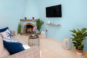 A living room with a brick fireplace, a flat-screen TV mounted on the wall, a sofa with blue cushions, and various potted plants. - Apartment 'Sea View Capistrano Village' with Sea View, Wi-Fi and Air Conditioning (Nerja)