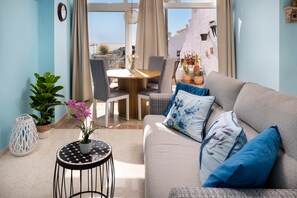 A living room with a sofa, a round table, and chairs. There is a view of buildings through a window.