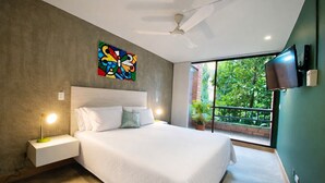 A modern bedroom with a large bed, a ceiling fan, a TV mounted on the wall, and a balcony with greenery visible through the window. - Modern 2BD apt near Provenza and Parque Lleras (Medellín)