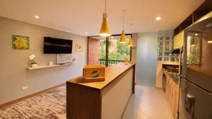 A modern kitchen with a wooden counter, a built-in stove, and a refrigerator. There is a TV mounted on the wall and a window with a view of greenery outside. - Modern 2BD apt near Provenza and Parque Lleras (Medellín)