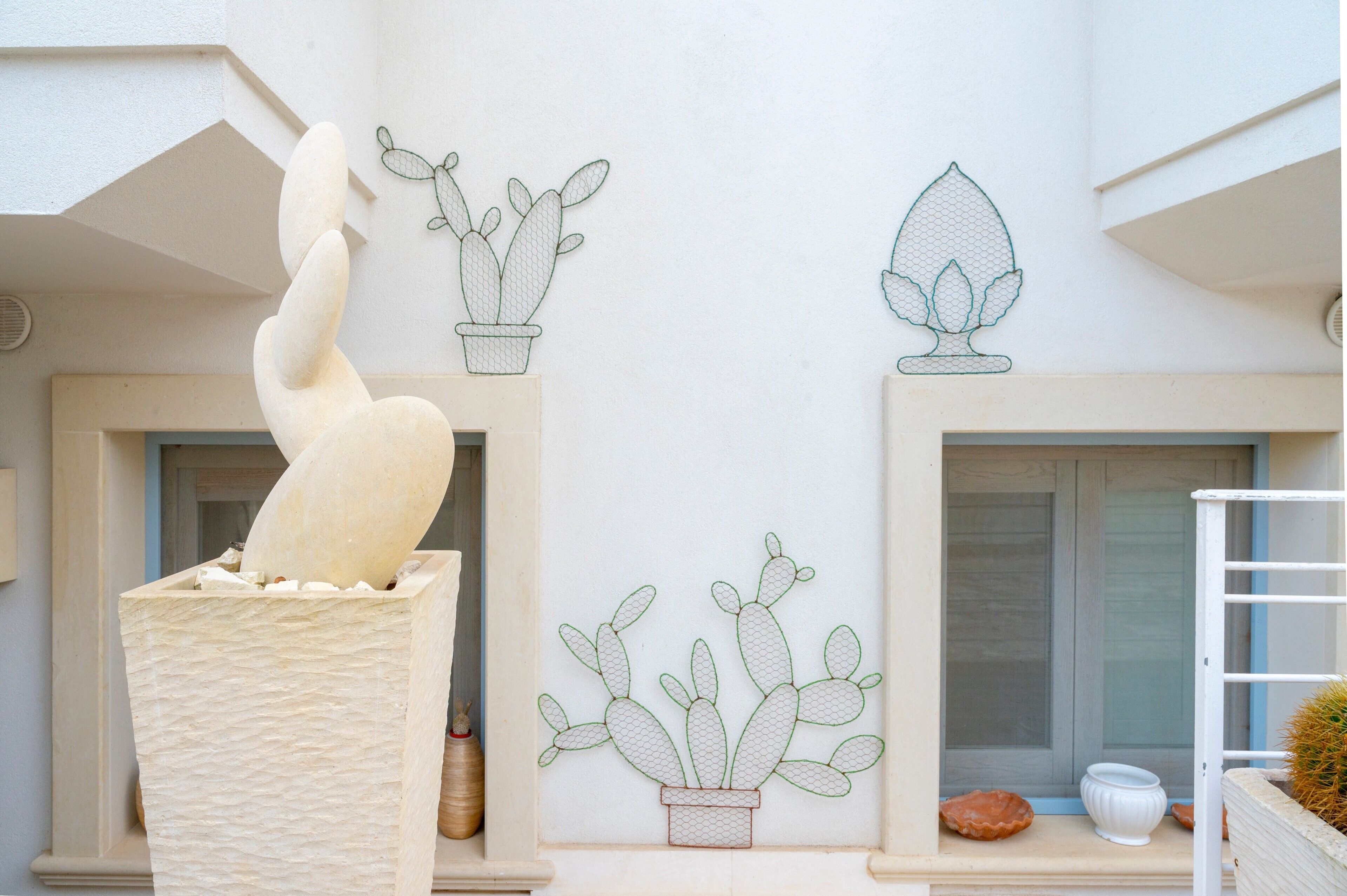 Ein Gebäude mit einer großen weißen Skulptur, Fenstern und Kaktus-Illustrationen an der Wand.