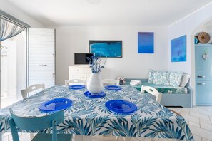 Un comedor con una mesa lista para cuatro, un jarrón blanco con ramas y un cuadro abstracto azul en la pared.
