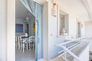Una habitación con una mesa de comedor, sillas, una barandilla blanca y una puerta con cortinas azules.