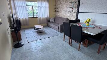 Un salon moderne avec un canapé, une table à manger et des chaises. On y trouve un ventilateur sur pied, une petite table et un vase décoratif avec des fleurs.