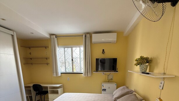 Een slaapkamer met een bed, nachtkastje, televisie en een ventilator.