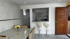 Een moderne keuken met een inbouwmagnetron, een houten deur en een eethoek met een glazen tafel en twee barkrukken.