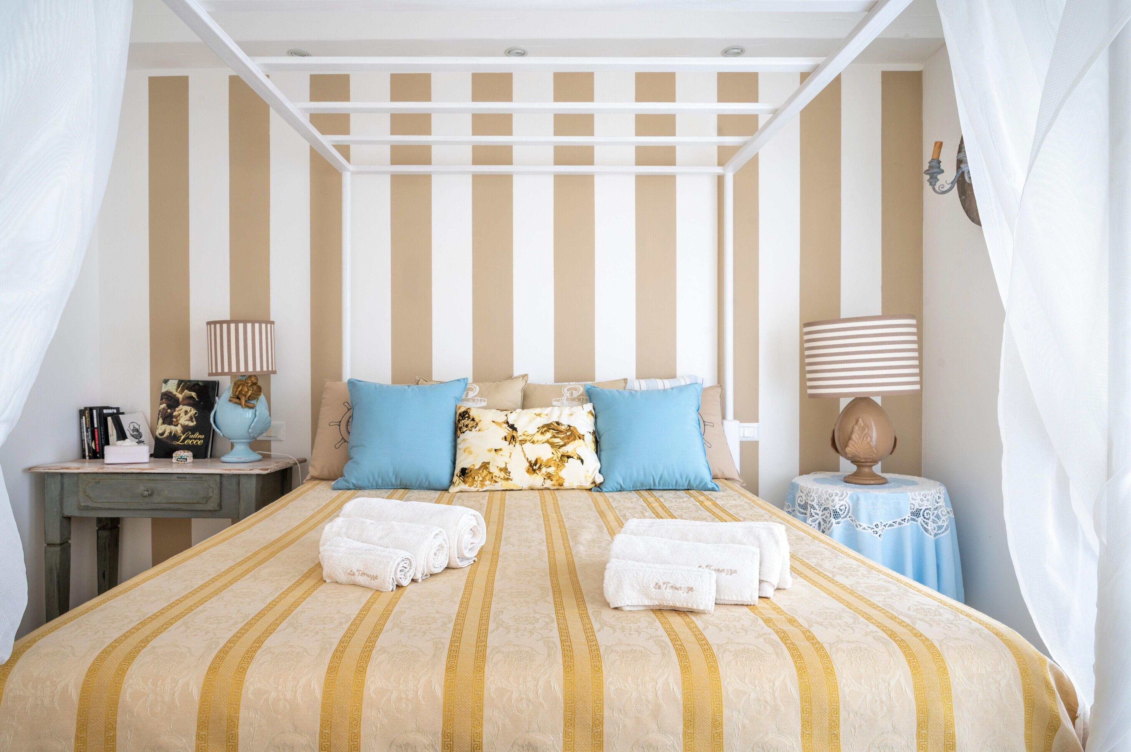 A bed with striped bedding, a nightstand with a lamp, and a small table with a decorative item.