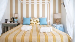 Uma cama com roupa de cama listrada, uma mesinha de cabeceira com uma luminária e uma pequena mesa com um objeto decorativo.