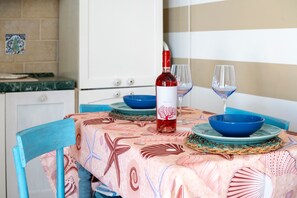 A dining table with a patterned tablecloth, a bottle of wine, two glasses, and blue bowls on a tiled backsplash.