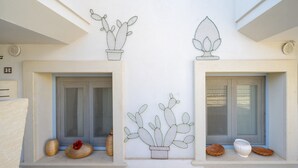 Fachada de edifício com duas janelas, cada uma decorada com um cacto em vaso.