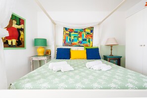 A bedroom with a green floral bedspread, a colorful abstract painting on the wall, and two bedside tables with lamps.