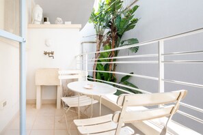 A balcony with a white metal railing, a small round table, two white chairs, a white bench, and a potted plant.