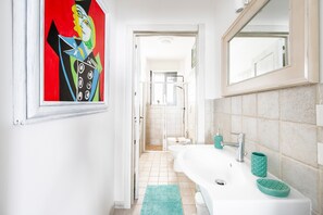 A bathroom with a white sink, a mirror, a shower, and a door leading to a hallway.