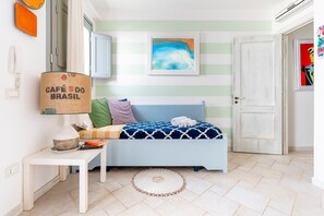 A room with a bed, a small table, a lamp, a framed picture, and a door.