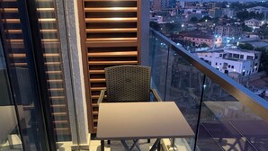 Un balcón con dos sillas de mimbre y una mesa, con vista a un paisaje urbano al anochecer.