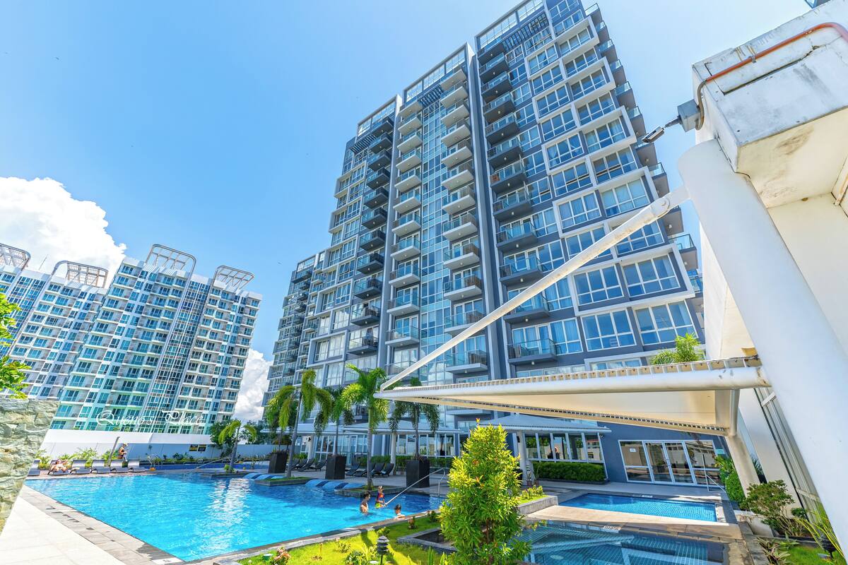 A modern high-rise hotel with a swimming pool, balconies, and lush greenery.