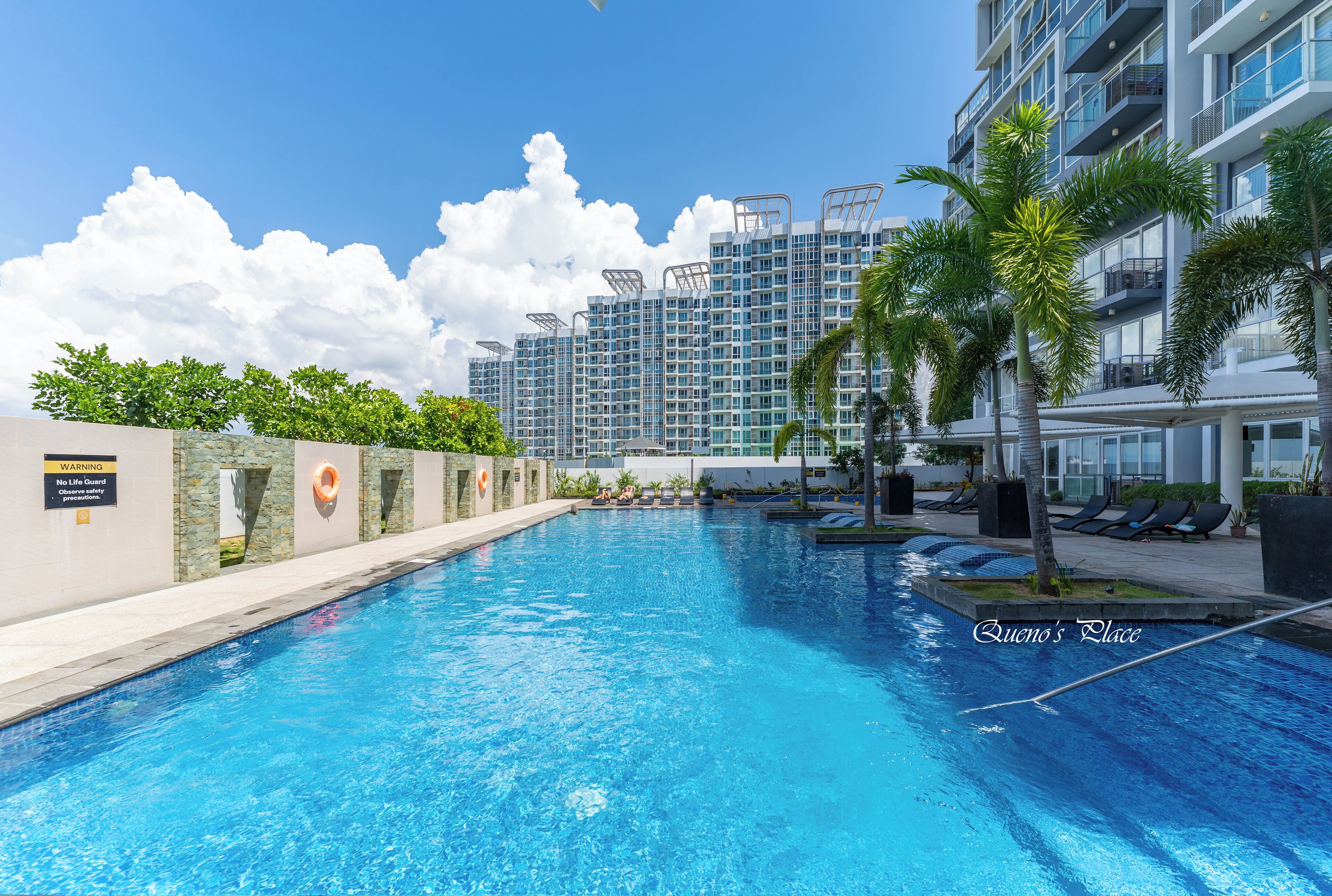 A swimming pool with lounge chairs and palm trees, surrounded by high-rise buildings.