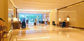Um hall amplo com piso lustroso, áreas de estar e balcão de recepção.