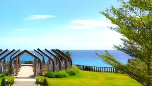 A modern building with a unique curved roof structure, a well-maintained lawn, and a view of the sea. - One Pacific Residence 1BR Ocean View (Lapu-Lapu)