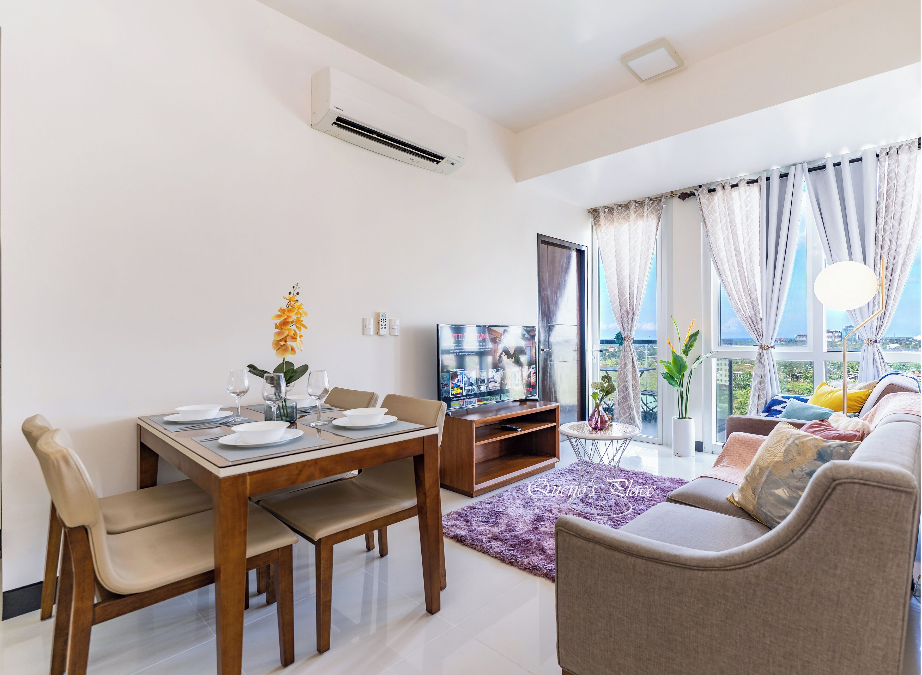 A modern living room with a dining area, a flat-screen TV, and a view of the city.