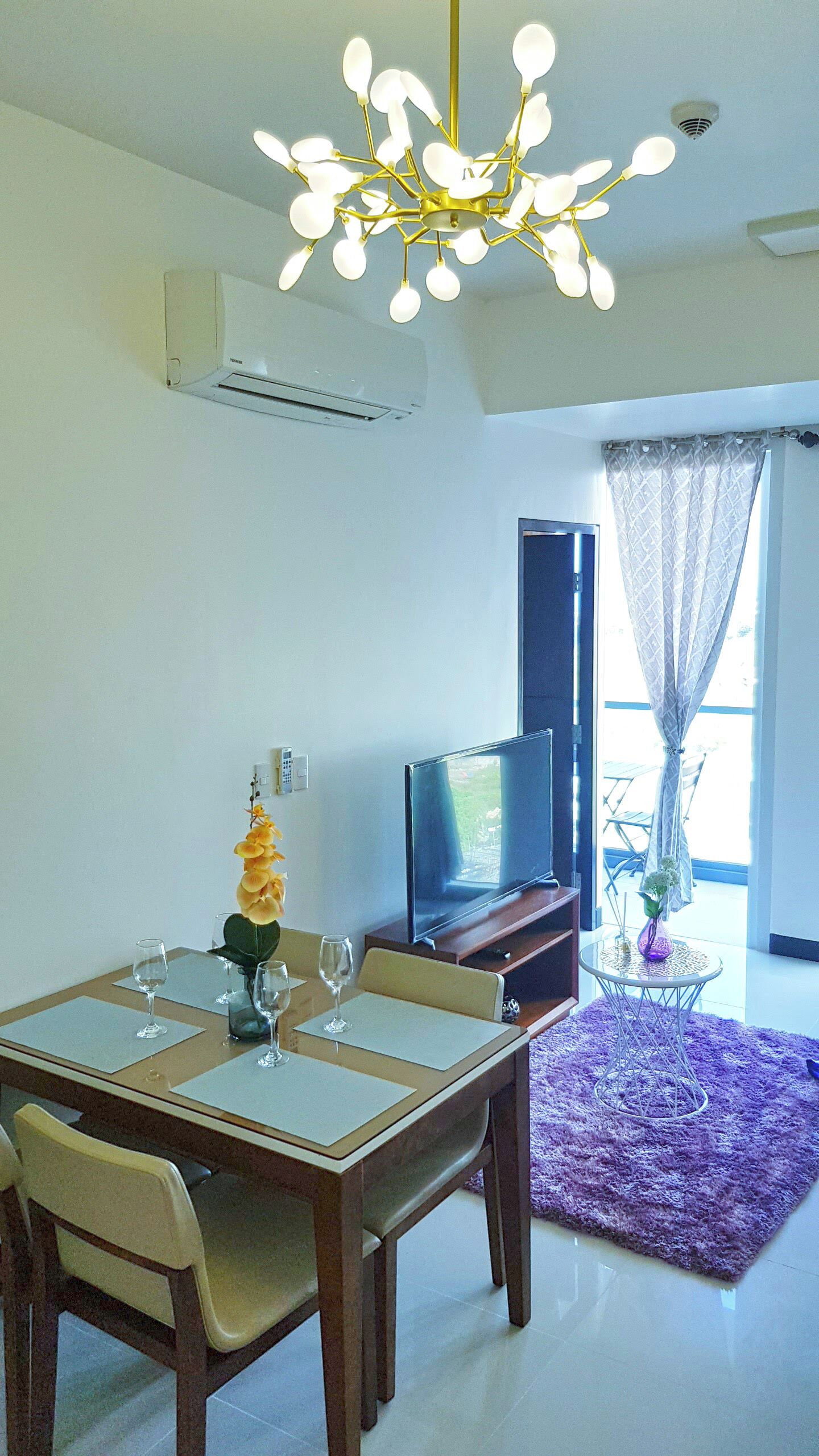 A dining area with a table set for four, a television, and a purple rug.