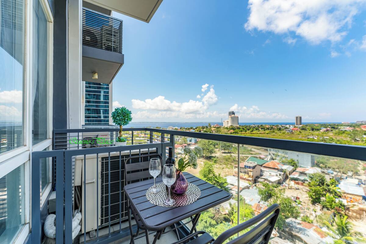 A balcony with a table set for two, a potted plant, and a view of the cityscape.