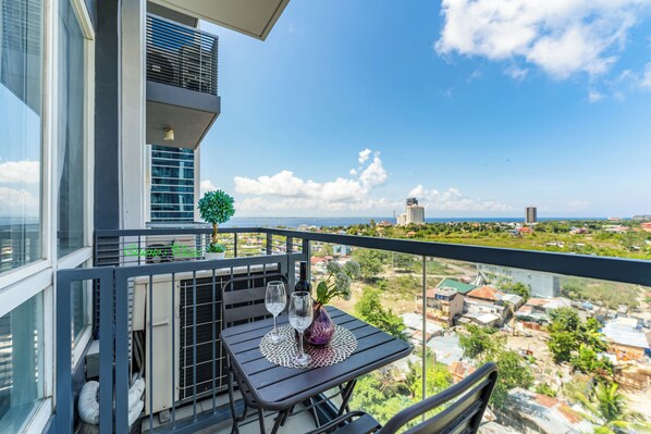 A balcony with a table set for two, a potted plant, and a view of the cityscape. - One Pacific Residence 1BR Ocean View (Lapu-Lapu)