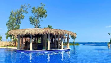 A poolside structure with a thatched roof, surrounded by a clear blue pool.