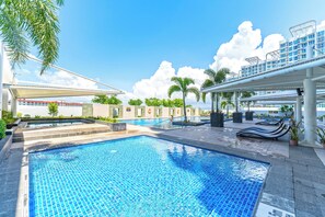Piscina com deck revestido, espreguiçadeiras e área coberta com vista para o mar.