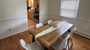 A dining area with a wooden table and white chairs, a kitchen in the background, and a window with blinds. - Hidden Gem Quiet Dead-End St Near All Casino (Montville)