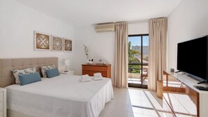 A hotel room with a bed, a TV, a desk, and a balcony with curtains. - 'Golden' Apartment with Shared Pool, Wi-Fi and Air Conditioning (Cabanas de Tavira)